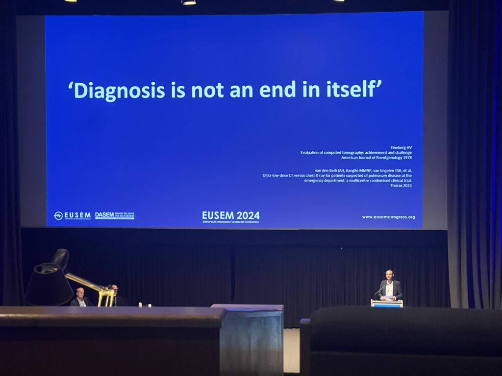 Stig Holm Ovesen presenting in front of one of his slides reading "Diagnosis is not an end in itself"
