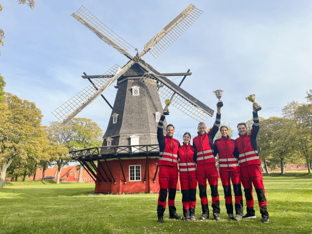 Winning Austrian EMS team holding up their trophies in front of a windmill in Copenhagen, Denmark